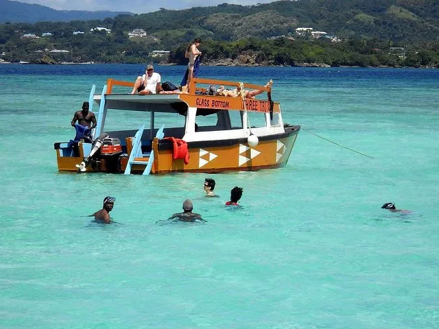 People swimming and relaxing around a glass bottom boat in clear turquoise water.