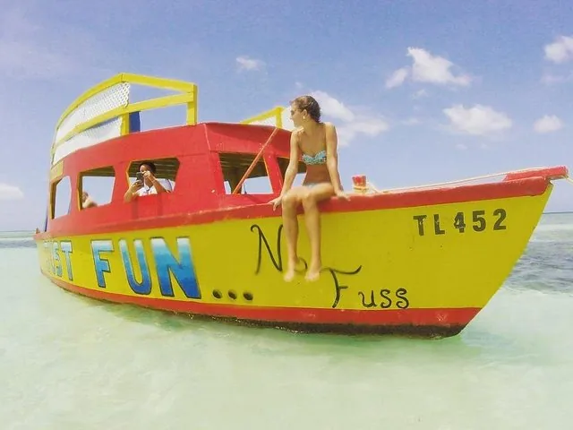 A woman sitting on the edge of a yellow and red boat in shallow water.