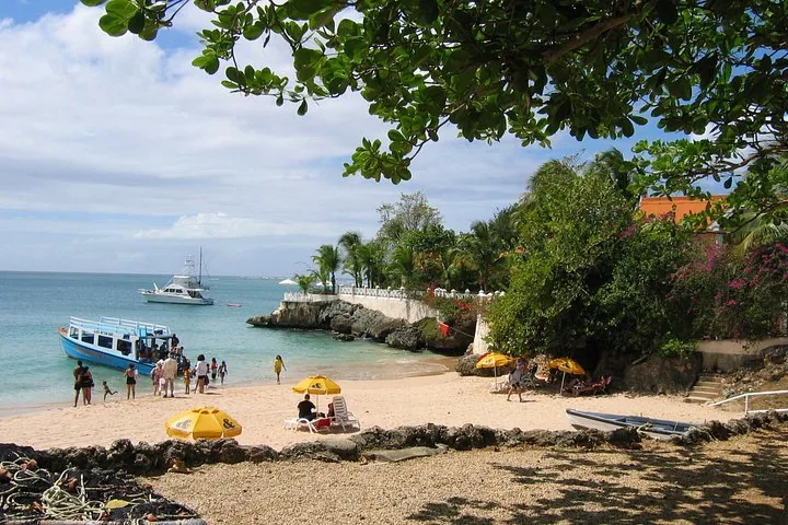A sandy beach with people, boats, and lush green trees along the shoreline.