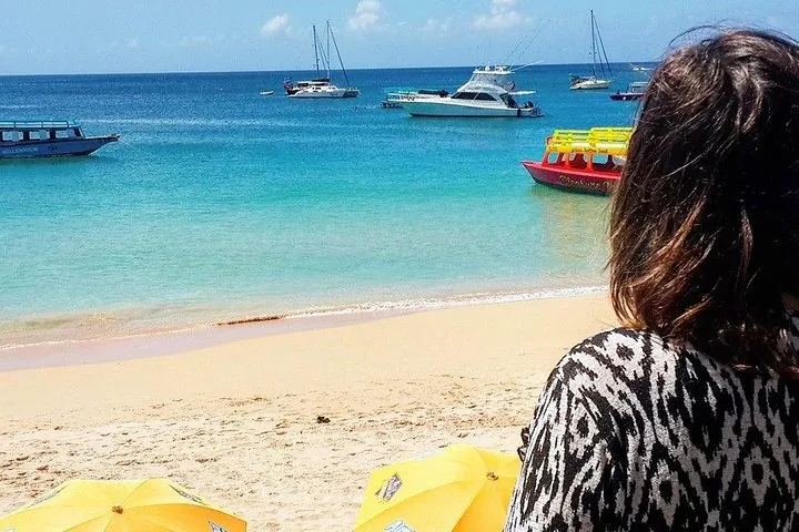 A person looking out at boats anchored in clear blue water from a beach.