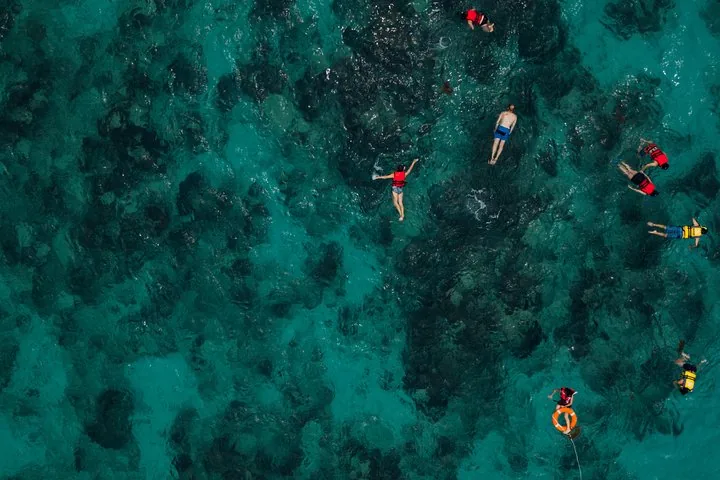 Aerial view of people snorkeling and swimming in clear turquoise water over coral reefs.
