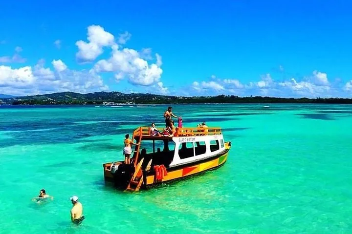 People swimming and relaxing around a colorful tour boat in bright turquoise water.